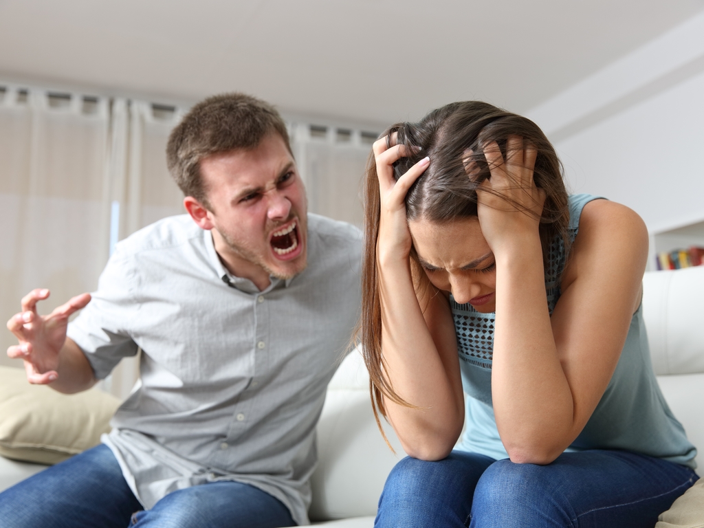 man screaming at woman while she holds her head