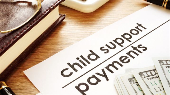 Child Support Payments paper with one hundred dollar bills stacked on top