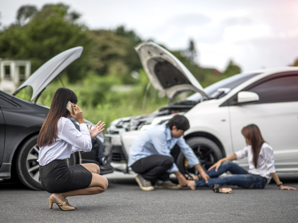 man attending to woman's leg after car accident while another woman is on the phone