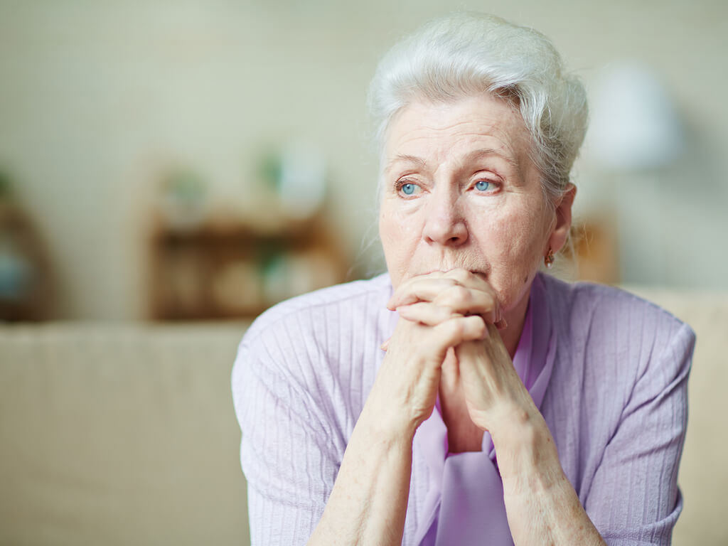 elderly woman with her hands crossed over her mouth