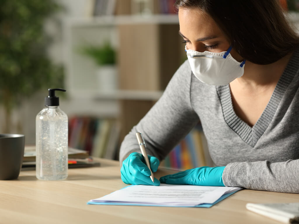 woman writing while wearing gloves and a face mask