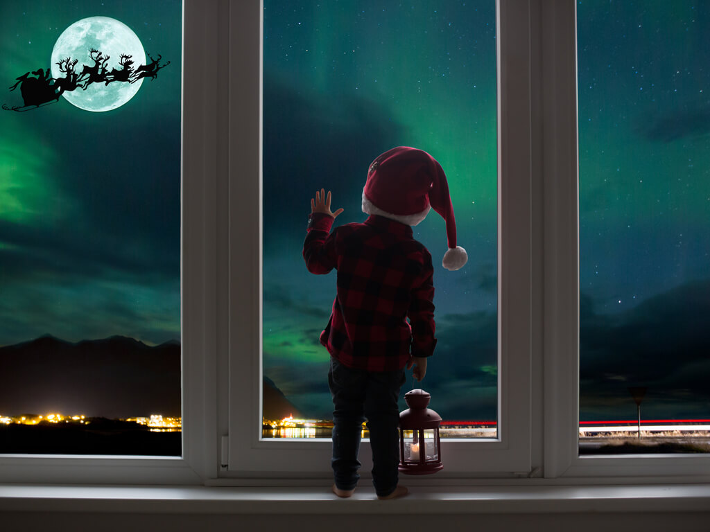 child standing alone in front of a window on christmas eve